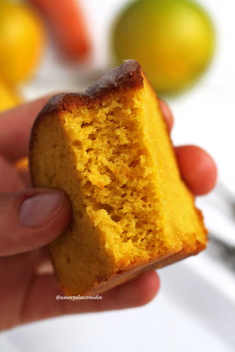 Mão segurando bolo de cenoura com laranja mostrando a textura macia e aerada do bolo