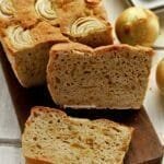 Pão de cebola sobre tábua de madeira retangular escura, sobre o pão fatias de cebola, o pão está fatiado com 1 fatia apoiada no pão cortado e a outra fatia deitada na tábua