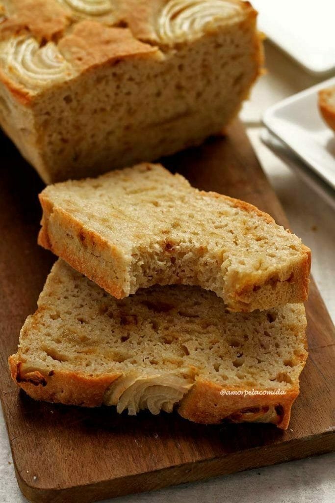 Duas fatias de Pão de cebola fatiadas e apoiado sobre uma tábua de madeira, a fatia de cima está mordida