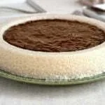 Bolo branco de tapioca com coco, na parte de cima do bolo tem uma piscina de calda de ameixa