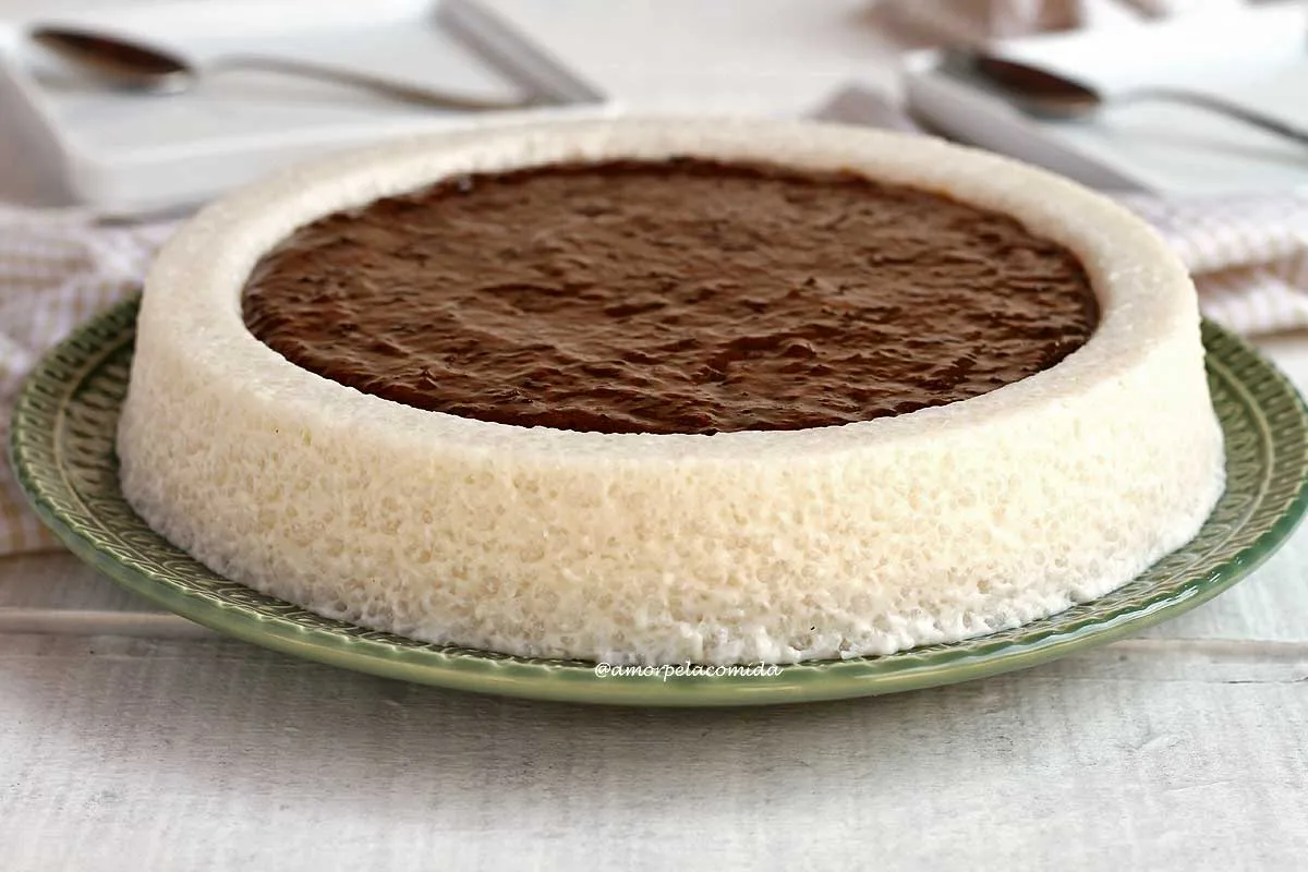 Bolo branco de tapioca com coco, na parte de cima do bolo tem uma piscina de calda de ameixa