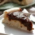 Fatia de bolo de tapioca com cobertura de ameixa preta sobre prato quadrado branco