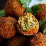 vários bolinhos de grão-de-bico amontoados em uma tigela verde, decorados com ramos de coentro fresco