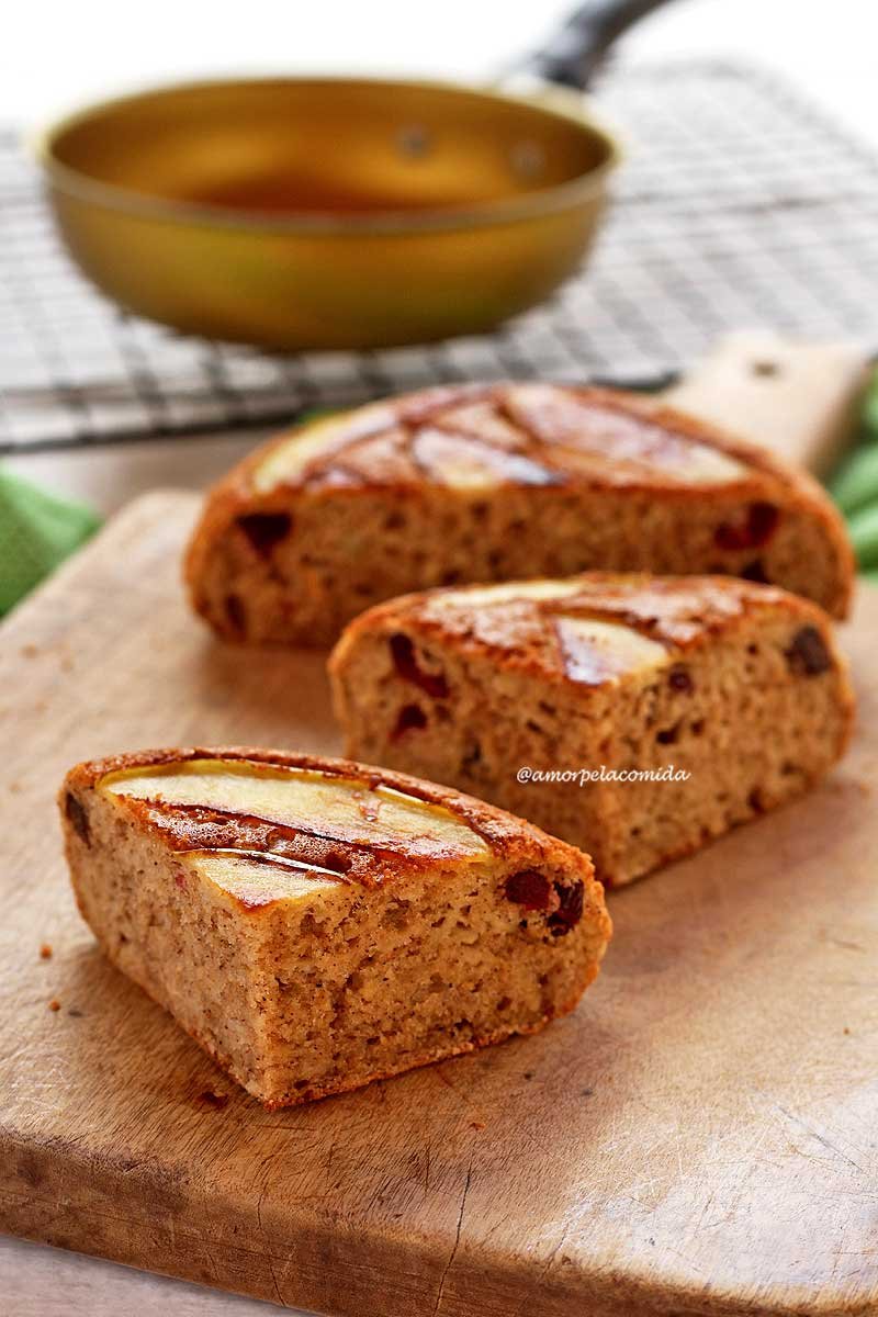 Bolo de maçã de frigideira partido ao meio e um dos pedaço novamente ao meio, sobre uma tábua de madeira