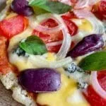 Pizza on a wooden board, topped with cheese, tomato, onion, basil and black olives