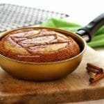 Frigideira dourada com bolo de maçã dentro sobre uma tábua de madeira em uma mesa branca