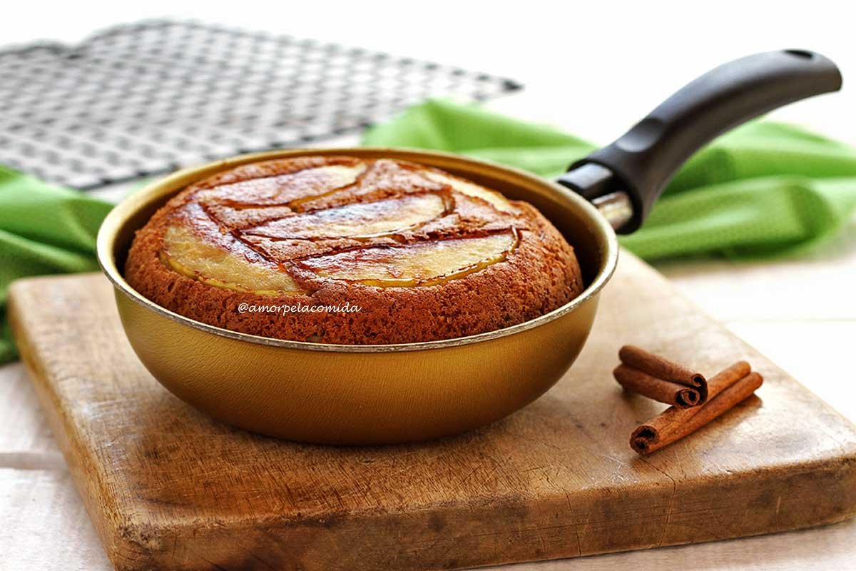 Frigideira dourada com bolo de maçã dentro sobre uma tábua de madeira em uma mesa branca