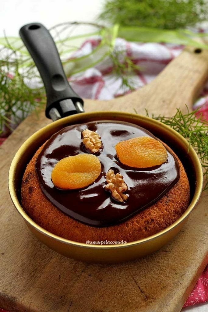 Frigideira pequena dourada sobre tábua de madeira, dentro um panetone decorado com cobertura de chocolate cremosa com damasco e nozes