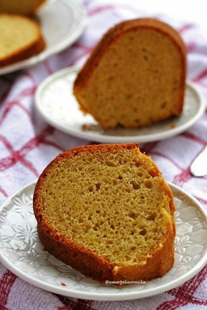 Duas fatias de bolo de fubá com batata-doce sobre prato branco redondo pequeno, a fatia da frente está deitada e a de trás está de pé