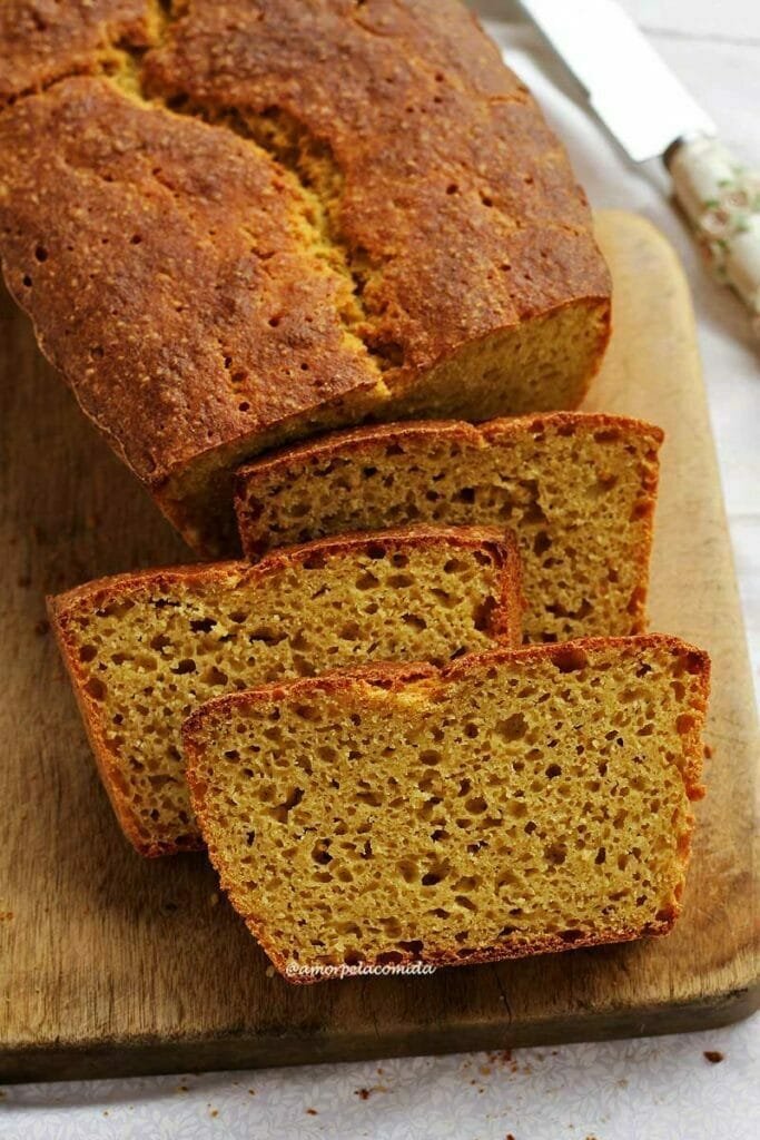 Três fatias de pão de fubá com batata-doce apoiados sobre o pão fatiado em uma tábua de madeira