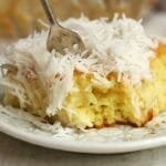 Pedaço de bolo de coco com cobertura de coco com garfo partindo o bolo e mostrando a textura macia e úmida da massa