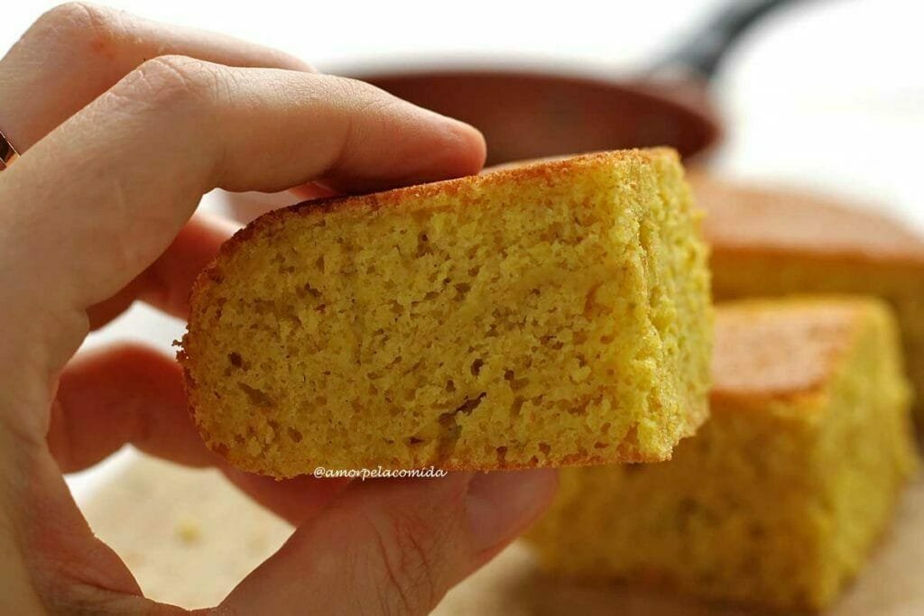 Mão segurando pedaço de bolo de laranja para mostrar a textura interna do pedaço que é aerada