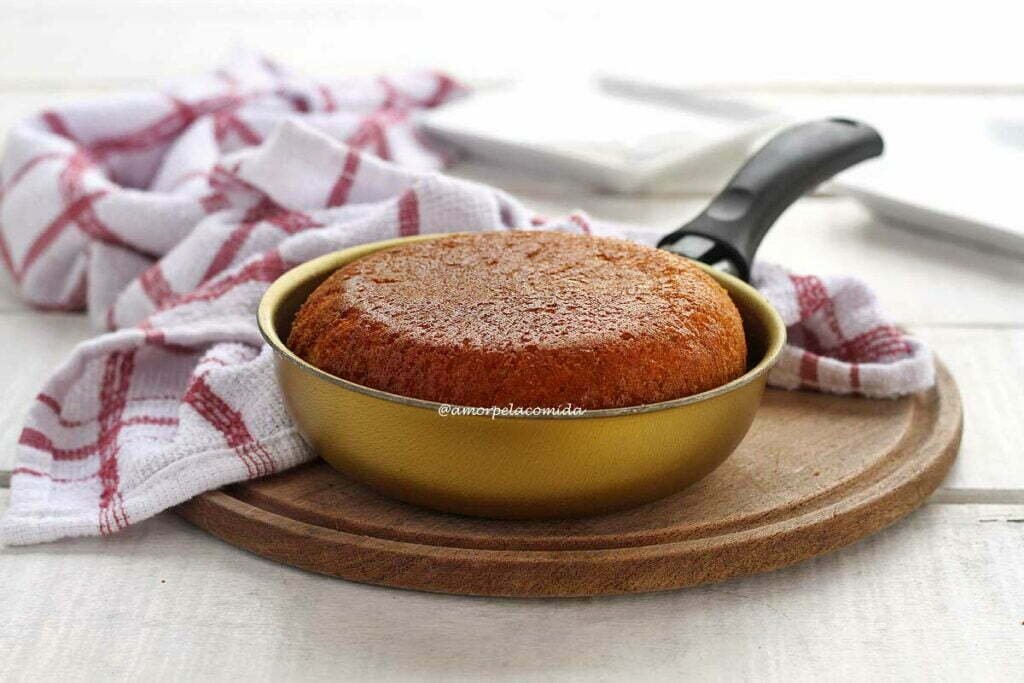 Frigideira pequena dourada com cabo preto sobre tábua de madeira com bolo de fubá dentro