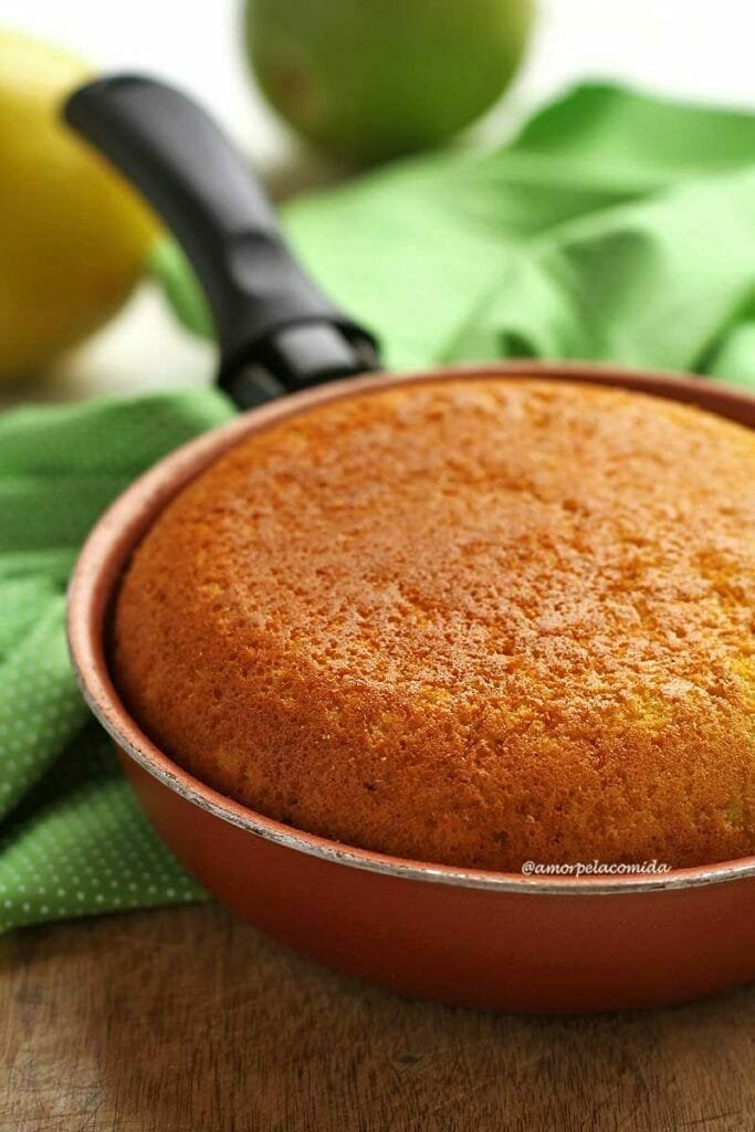 Frigideira marrom com cabo preto, dentro um bolo de laranja. A frigideira está sobre um pano verde claro