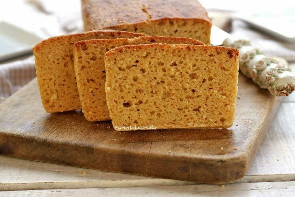 Pão com três fatias cortadas apoiadas sobre o pão de mandioca em uma tábua de madeira