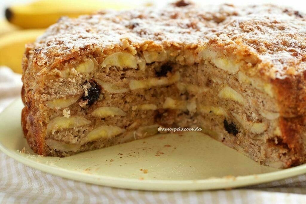 Torta de banana cortada mostrando as camadas internas de banana, algumas passas e a cobertura de aveia com açúcar polvilhado