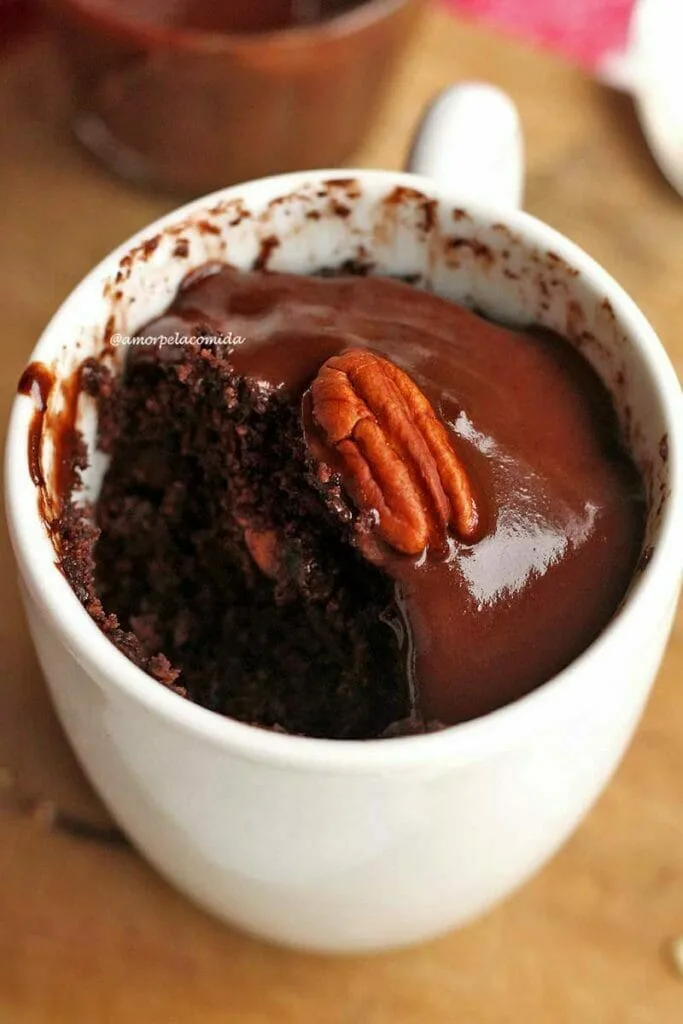 Taza blanca con pastel de chocolate adentro, encima del pastel un glaseado de chocolate y una nuez pecana, el pastel ya está parcialmente comido