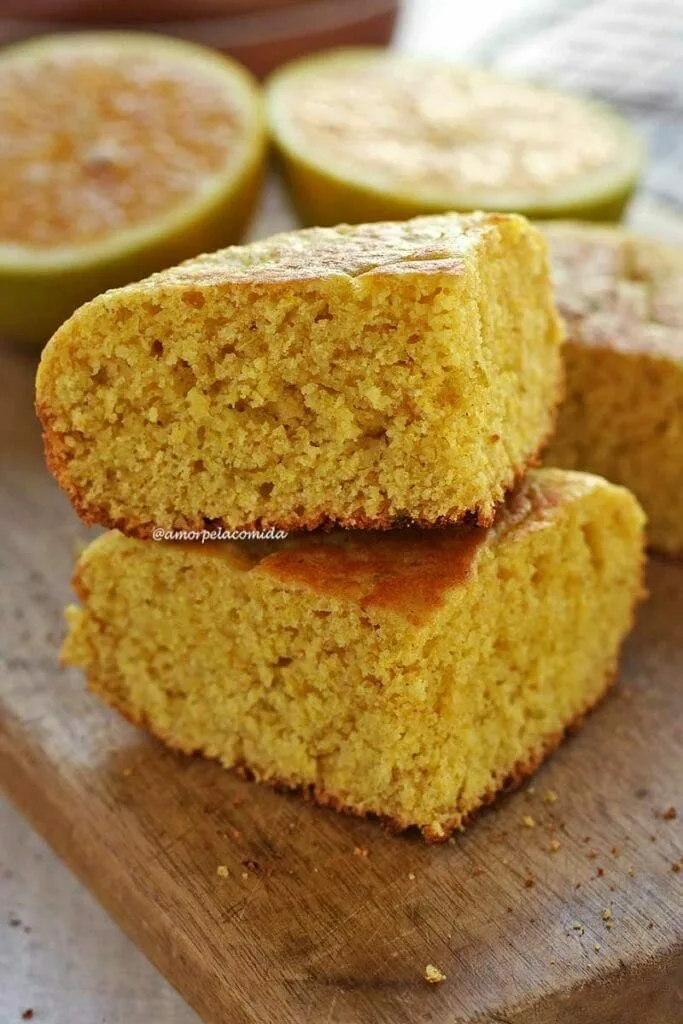 Dois pedaços de bolo de laranja sobrepostos em uma tábua de madeira de cor clara em uma mesa branca