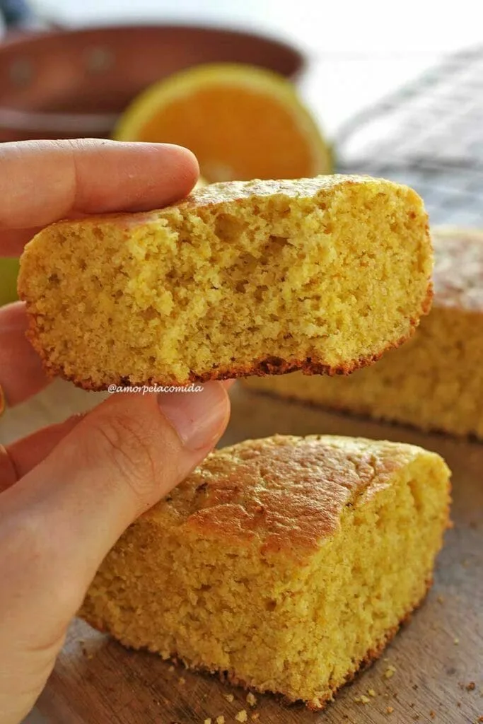 Mão segurando pedaço mordido de bolo de laranja de frigideira