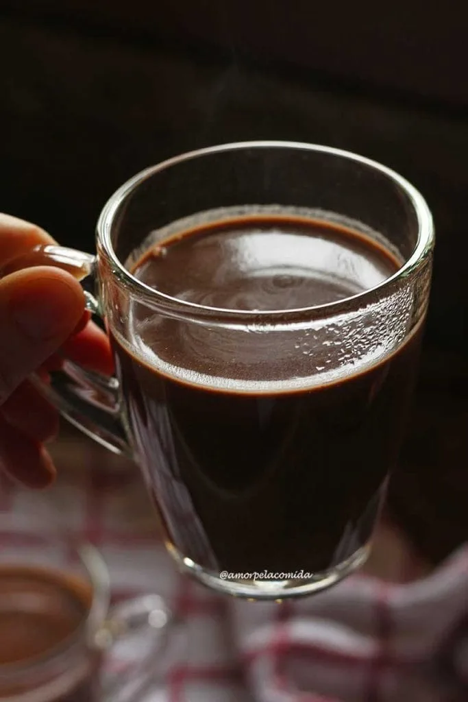 Mano sosteniendo una taza de vidrio transparente con chocolate caliente dentro