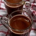 Duas xícaras de chocolate quente sobre pano branco e vermelho quadriculado
