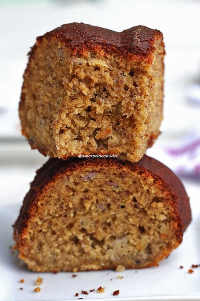 Dois pedaços de bolo de banana sobrepostos, o pedaço de cima está mordido mostrando a textura aerada do bolo