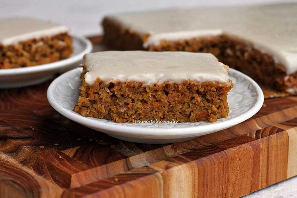 Pedaço de bolo de cenoura com cobertura branca sobre tábua de madeira