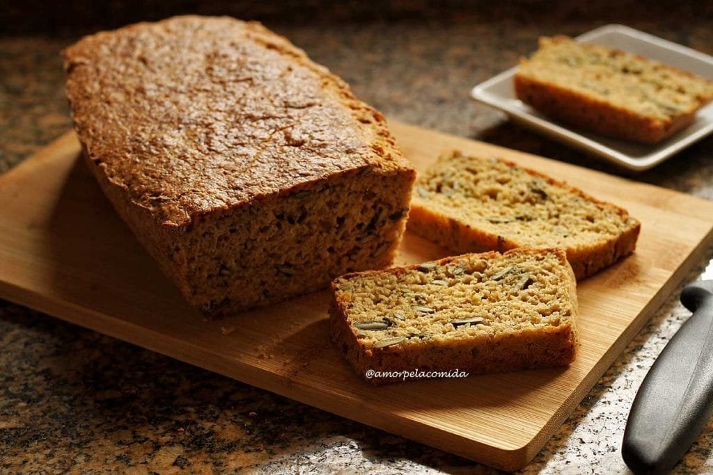 Pão caseiro sobre tábua de bambu já fatiado. Ao lado do pão duas fatias deitadas sobre a tábua