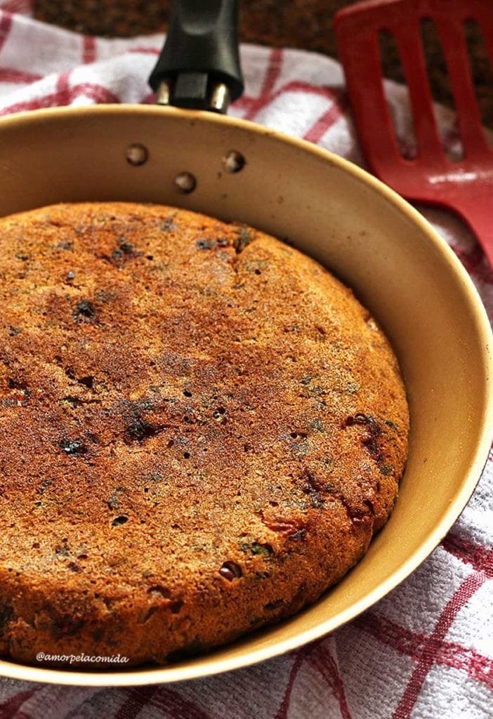 Torta salgada de sardinha dentro de uma frigideira média, abaixo um pano de prato branco com xadrez vermelho