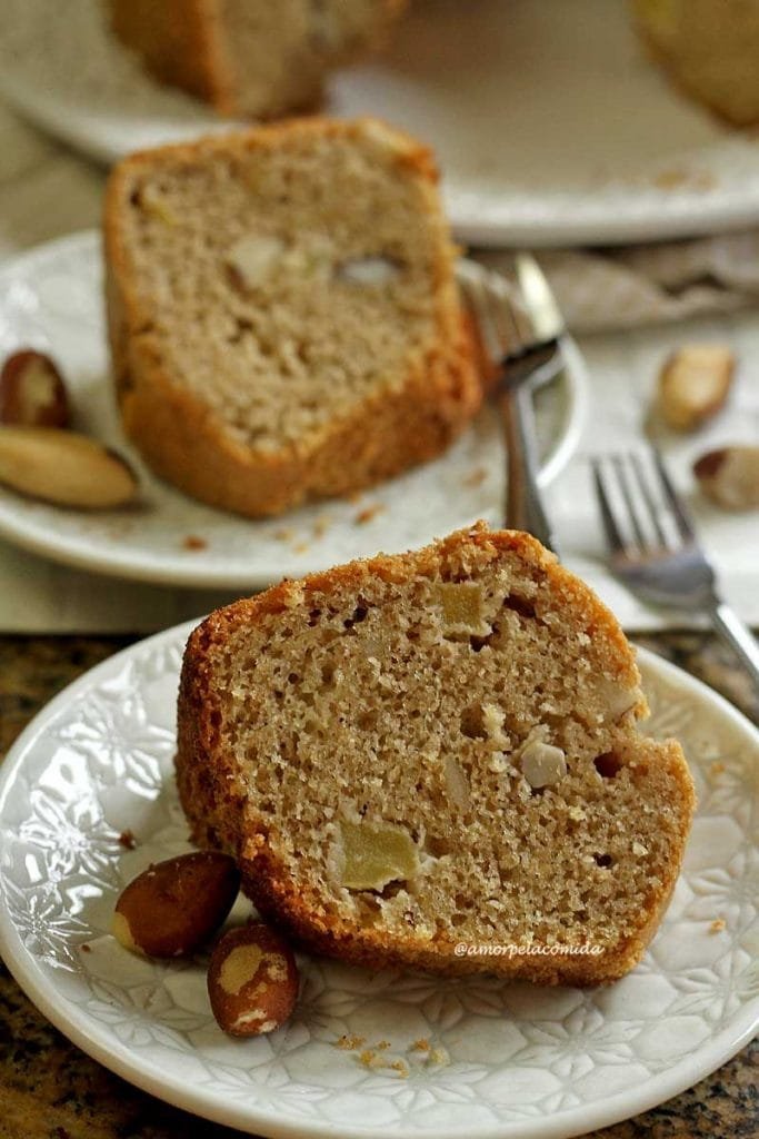 Duas fatias de bolo de castanha sobre pratos redondos pequenos, ao lado algumas castanhas do pará e dois garfinhos