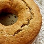 Bolo redondo com furo no meio sobre prato branco com detalhes em relevo na borda, o topo do bolo apresenta uma rachadura característica de bolos caseiros