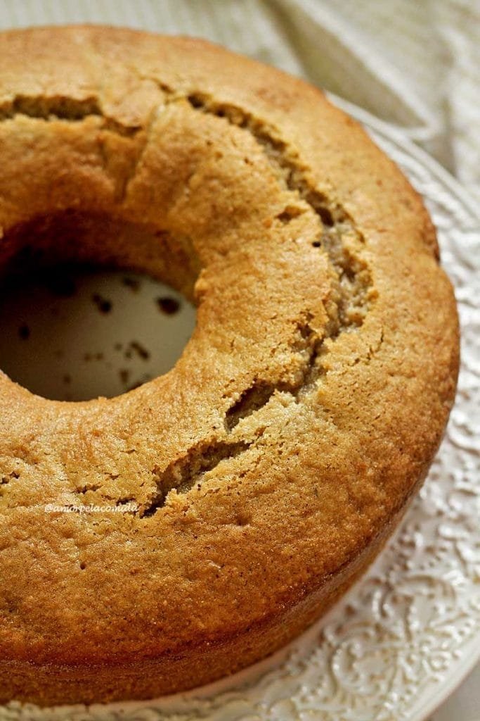 Gâteau rond avec trou au milieu sur une assiette blanche avec détails en relief sur le bord, le dessus du gâteau présente une fissure caractéristique des gâteaux faits maison