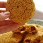 Mão segurando broa de fubá com pontinhos de goiabada saindo dela, abaixo um prato com várias broas