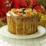 Panetone sobre prato branco com cobertura de glacê de açúcar e frutas cristalizadas no topo