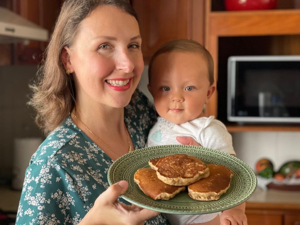 Mãe segurando um bebê de 9 meses e um prato de panqueca de banana