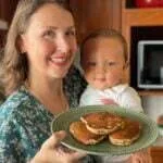 Mãe segurando um bebê de 9 meses e um prato de panqueca de banana