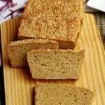 Três fatias de pão apoiadas sobre o pão que no topo tem gergelim e está sobre uma tábua de madeira