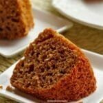 Fatia de bolo de batata doce deitada sobre prato quadrado branco, ao fundo mais uma fatia sobre um prato e uma parte do bolo que foi partido