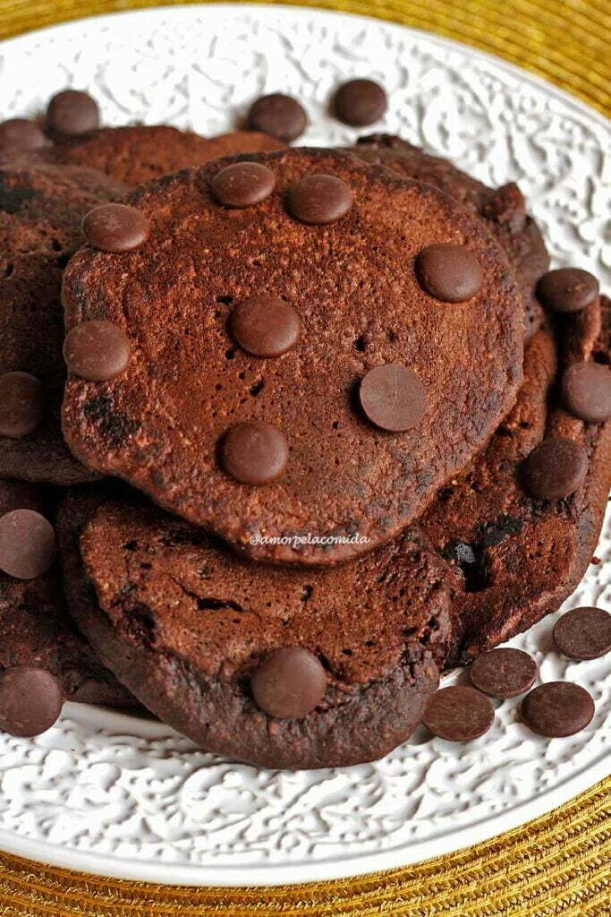 Várias panquecas de chocolate amontoadas sobre prato branco, sobre as panquecas gotinhas de chocolate para enfeitar