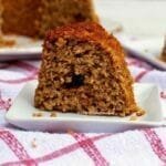 Pedaço de bolo de maçã sobre prato quadrado pequeno, ao fundo o bolo partido