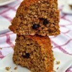 Dois pedaços de bolo de maçã com aveia empilhados sobre prato branco quadrado pequeno