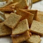 Vários biscoitos quadrados saindo de um vidro deitado sobre jogo americano branco