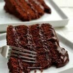 Duas fatias de bolo de chocolate recheado, com 3 camadas de recheio e um garfo fazendo o movimento de tirar uma garfada