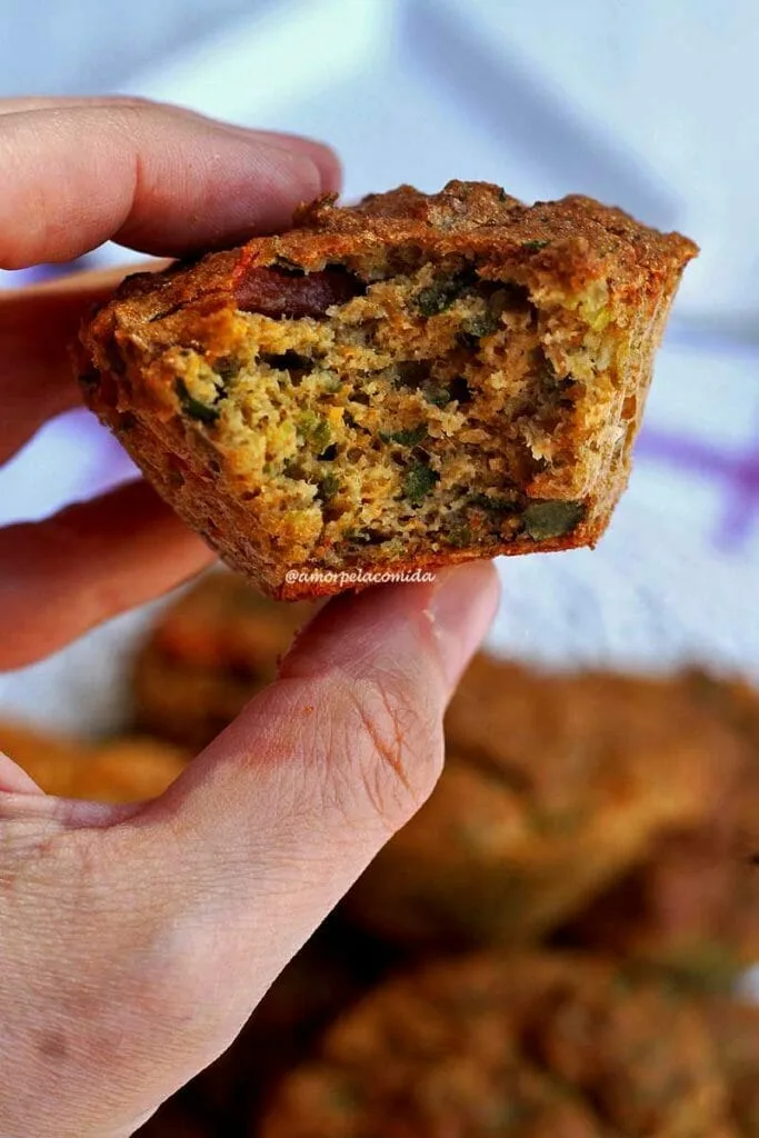 Mão segurando bolinho salgado de atum com vegetais, o bolinho está mordido mostrando a parte interna do bolo salgado