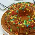 Bolo redondo com furo no meio coberto com cobertura cremosa e caramelizada com pequenos confeitos de chocolate colorido por cima para decorar o bolo