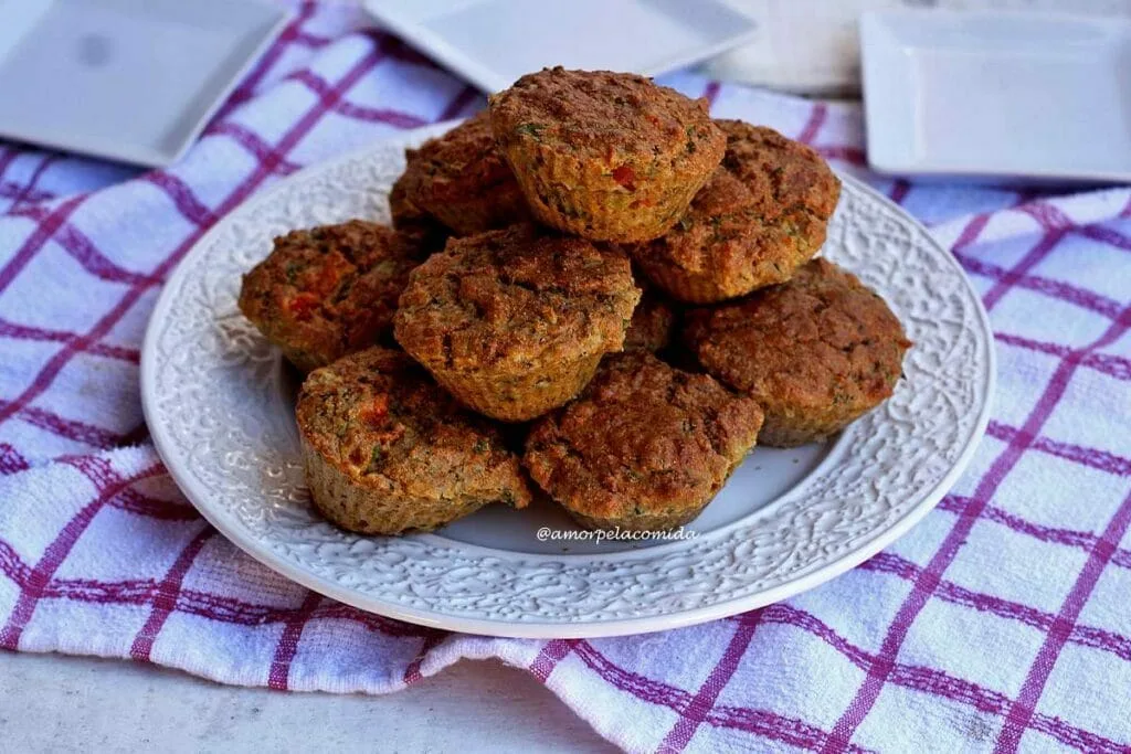 Vários muffins salgados empilhados sobre um prato redondo grande sobre uma toalha branca com xadrez vermelho