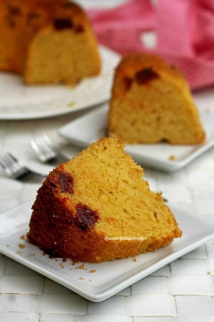 Duas fatias de bolo de fubá com pedacinhos de goiabada, a fatia da frente está deitada sobre o prato e a de trás está de pé