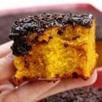 Mão segurando pedaço quadrado de bolo de cenoura com cobertura de chocolate que foi mordido