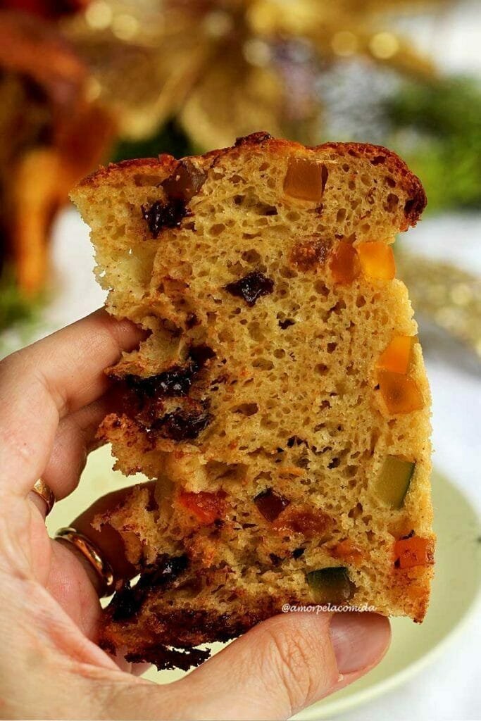 Mão segurando fatia de panetone com frutas e algumas gotas de chocolate