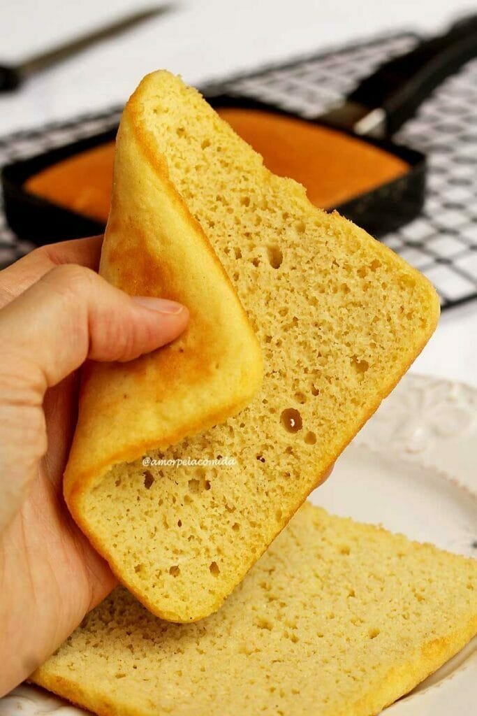 Mão segurando fatia quadrada de pão, a fatia está sendo dobrada com o polegar